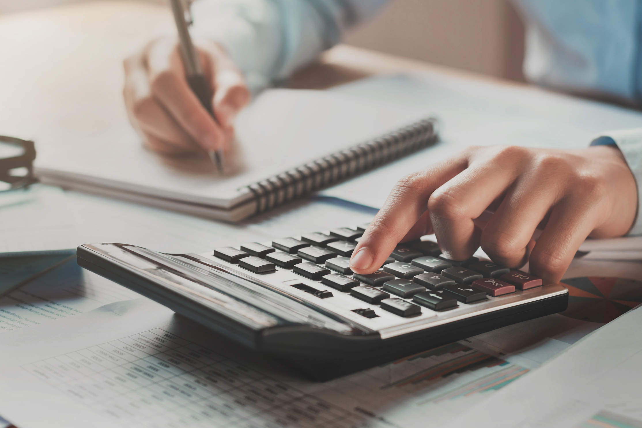 businesswoman working in office on desk using calculator and pen with sunshine